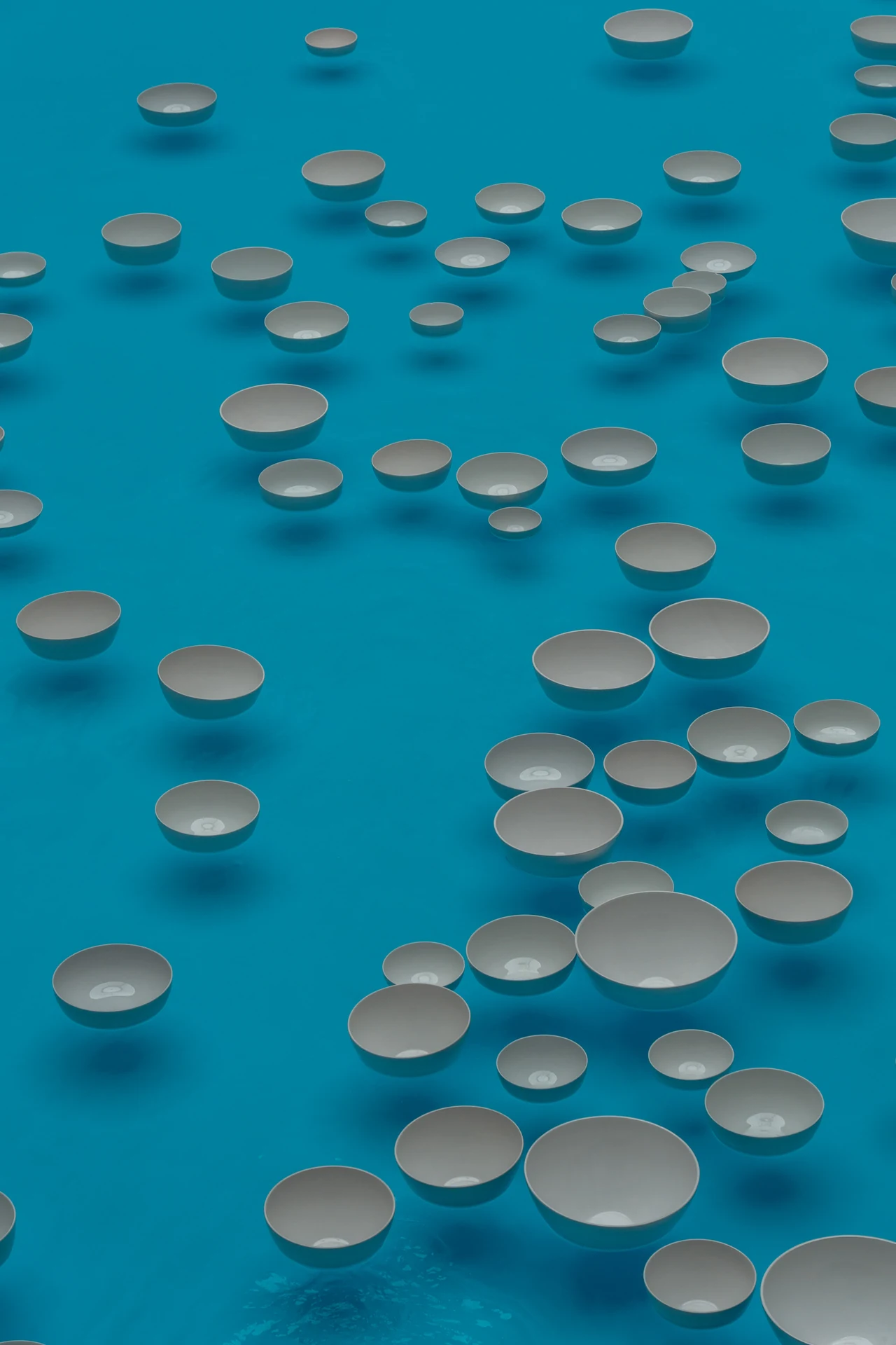 White bowls floating on turquoise water in an installation at the Bourse de Commerce.