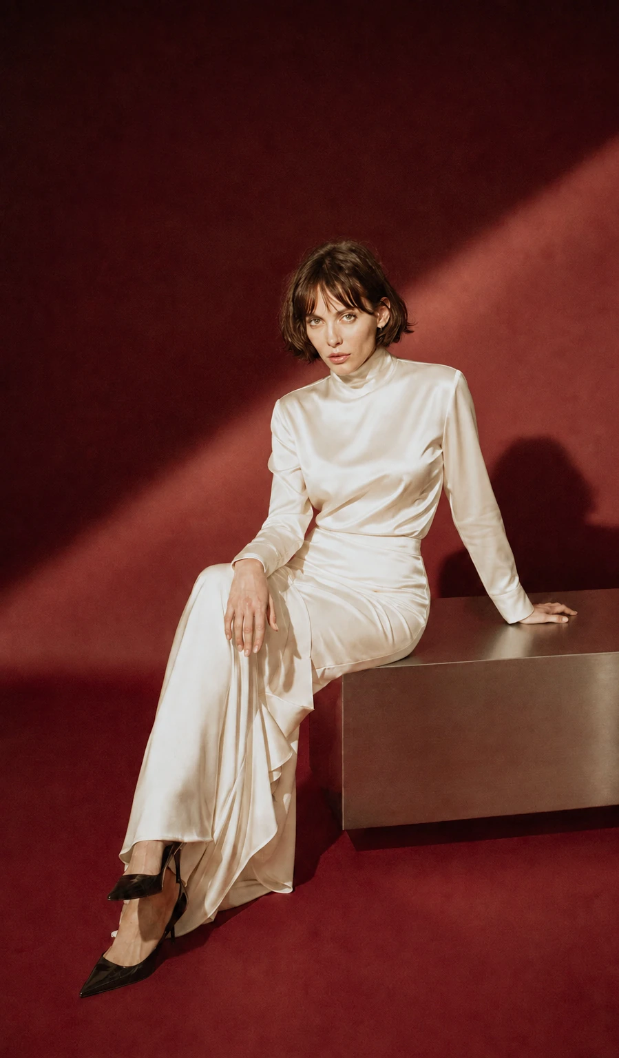 Ivory satin outfit against a deep red wall.