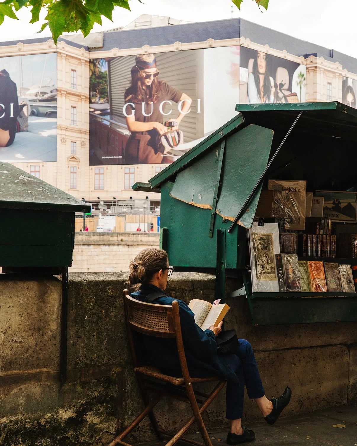 A reader seated beside a green bookstall in Paris.